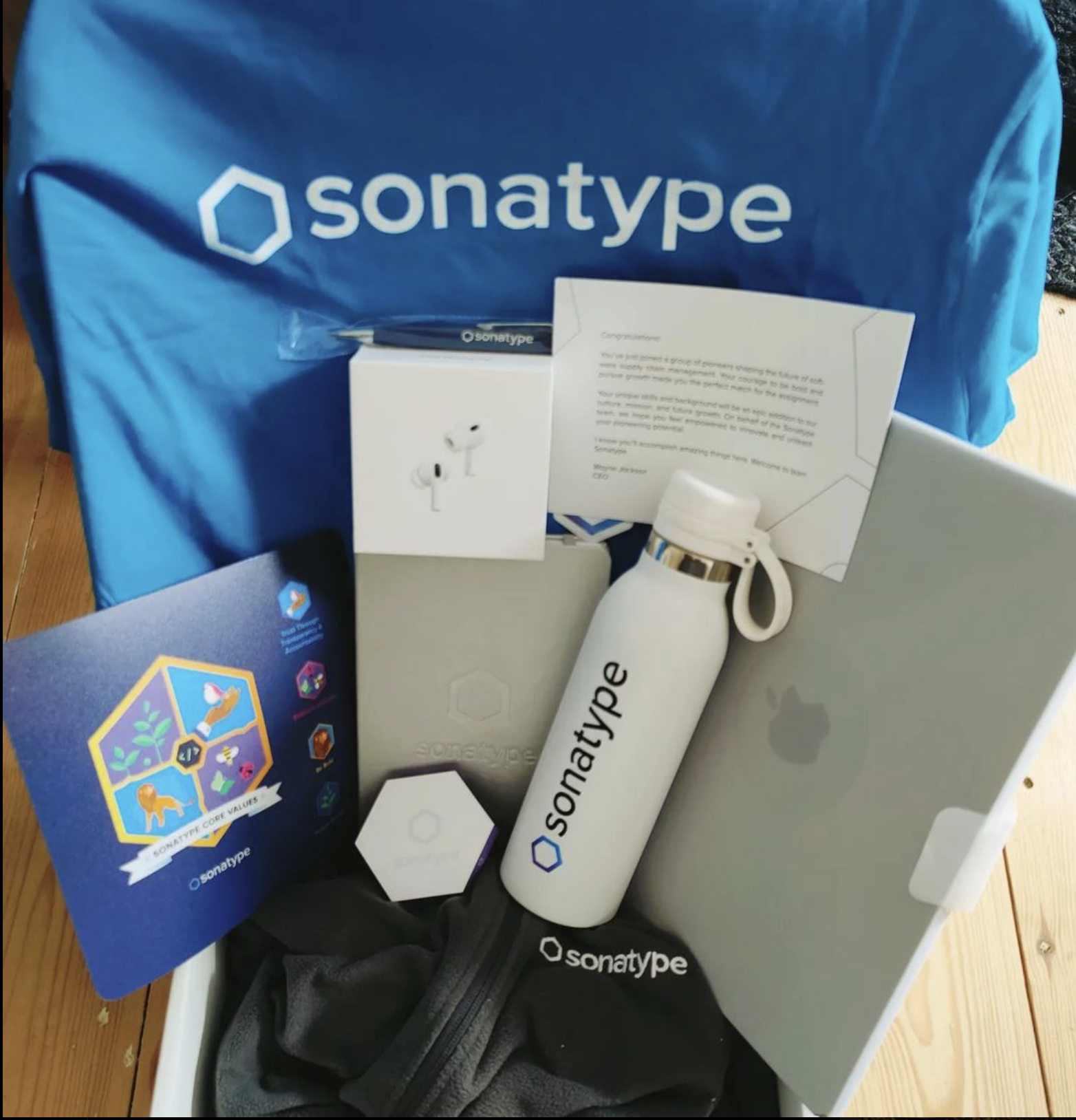 Sonatype swag of t-shirt, water bottle, mousemat, laptop, Airpods and various drawing items.